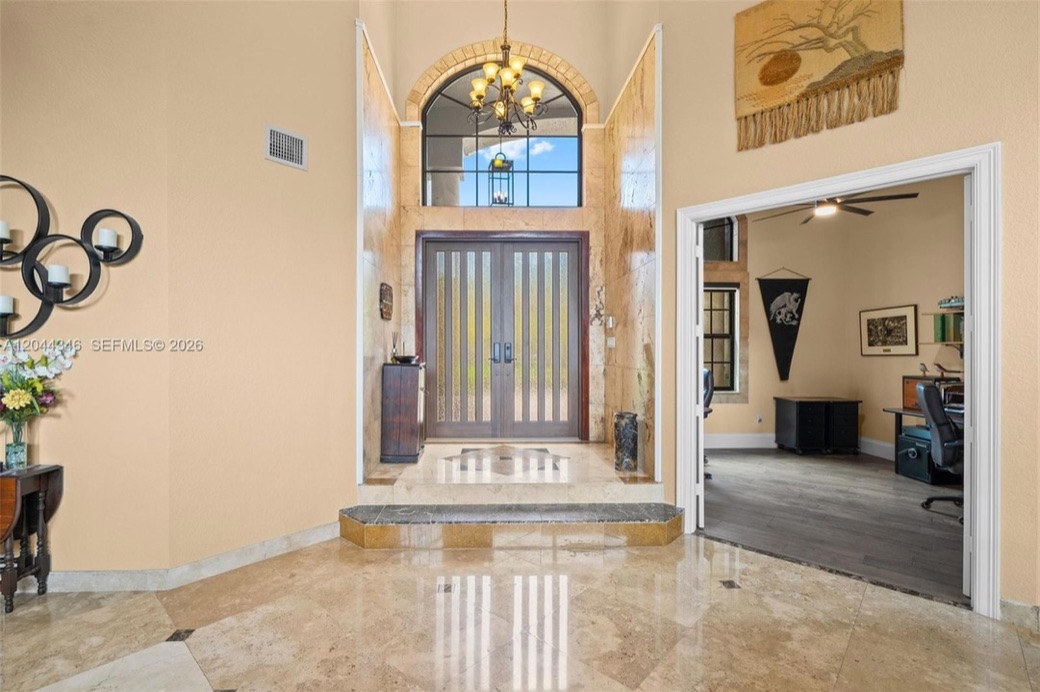 Two-story marble entry foyer with an iron chandelier and carved wood double front doors