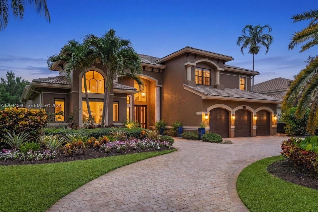 Twilight exterior of 2982 East Lake Vista Circle in Davie — glowing windows, a three-car garage and a curved paver driveway framed by palms against a deep-blue dusk sky